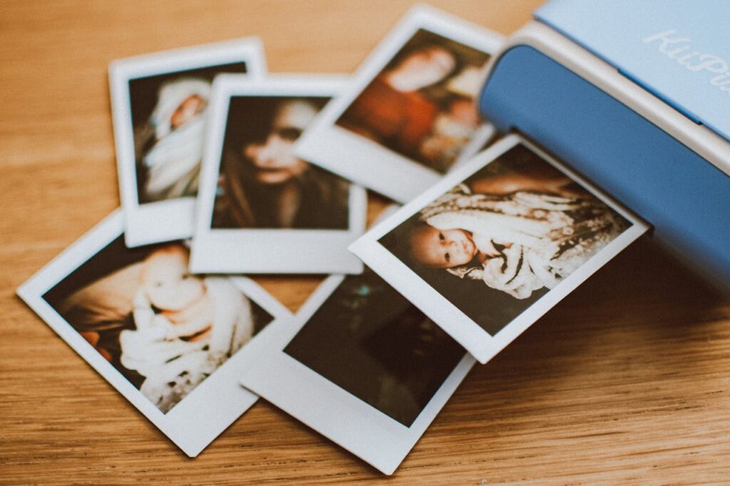 A collection of instant photo prints scattered on a wooden table, featuring personal moments.